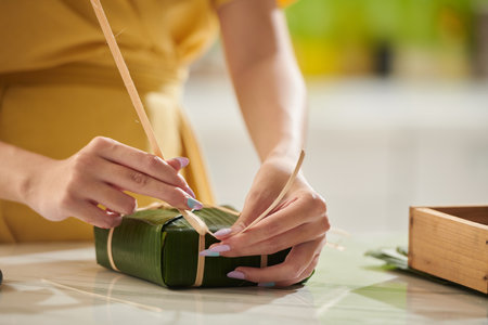 Closeup image of young woman wrapping traditional rice cake in banana leavesの写真素材