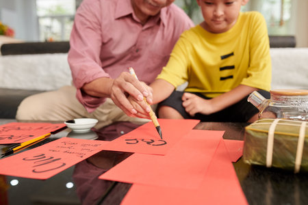 Senior man teaching granson to create greeting cards for Chinese New Year