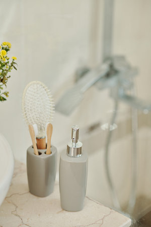 Liquid soap dispenser and cup with toothbrushes next to sink in bathroom