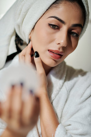 Young woman in bathrobe applying makeup after morning shower