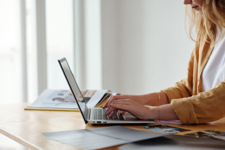 Closeup image of art gallery owner working on laptop at desk answering e-mails from artists and...