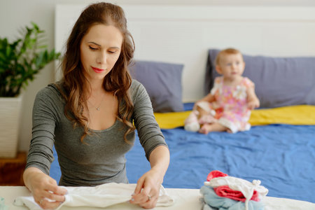 Young woman ironing and folding clothes when her daugher playing in backgroundの写真素材