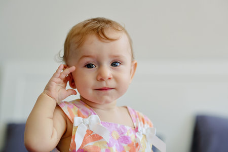 Portrait of little blond girl touching her ear and looking at cameraの写真素材