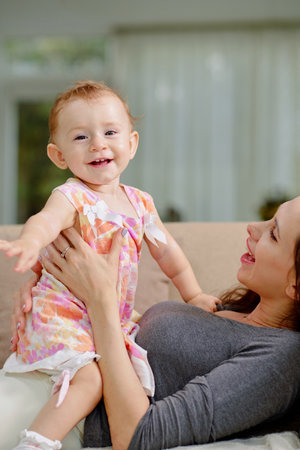 Cheerful young woman looking and laughing baby girl sitting on her stomachの写真素材
