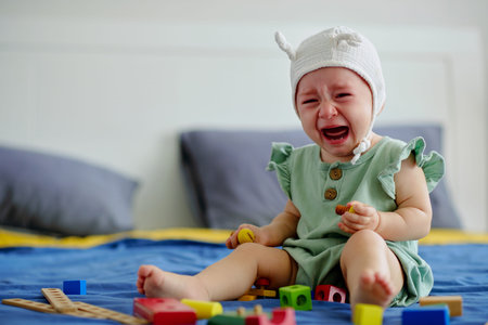 Little girl sitting on bed of parents with many toys and crying
