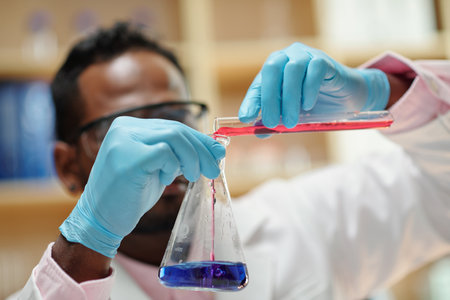 Close-up image of scientist pouring red reagent in flask with bue liquidの写真素材
