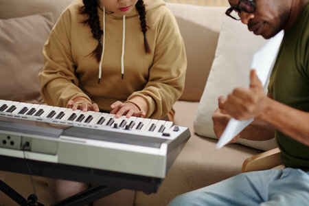 Teenage girl leaning playing synthesizer with private teacherの写真素材