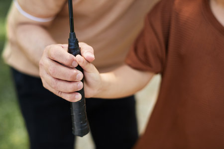 Grandfather explaining kid how to hold badminton racketの写真素材
