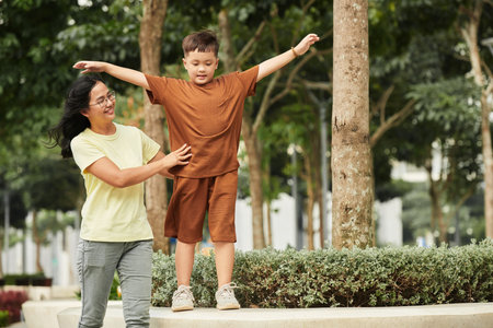 Mother supporting preteen son walking along flowerbedの写真素材