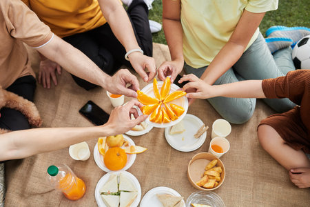 Hands of family members taking slices of orange from plate, view from aboveの写真素材