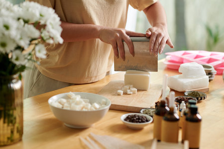 Hands of woman using metal cutter when cutting soap base in small cubes for meltingの写真素材