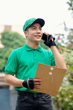 Portrait of delivery man with packed documents talking on phone with client