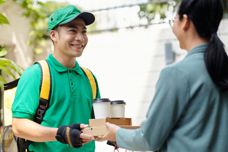 Happy courier giving order to customer meeting him in doorwaysの写真素材