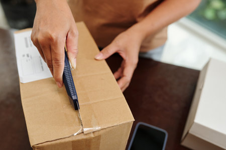 Hands of person opening parcel with office knifeの写真素材