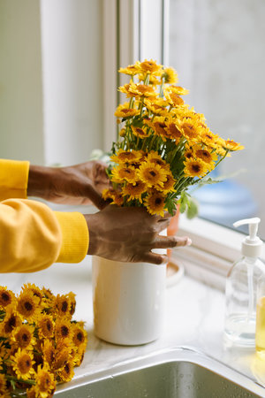 Hands of Black woman putting freshly cut yellow flowers in vase on window sillの写真素材