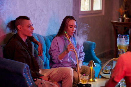 Young woman smoking hookah when hanging out with friends in bar