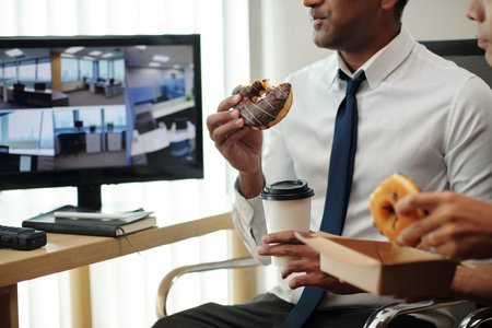 Cropped image of security guards eating sweet donuts when watching surveillance footage on screensの写真素材