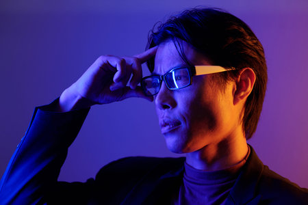 Portrait of confident young man adjusting glasses and looking away