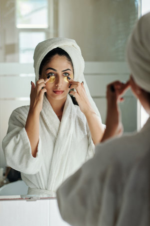 Young woman in bathrobe applying brightening eye patchesの写真素材