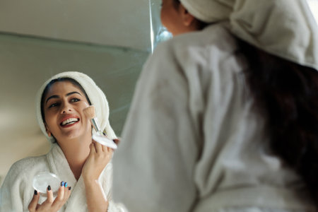 Joyful young woman in bathrobe applying face powderの写真素材