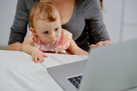 Curious little girl looking at laptop screen when her mother working from homeの写真素材