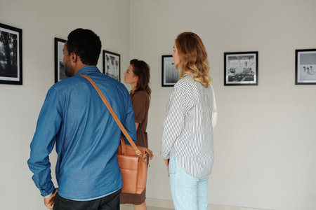 Group of intercultural students or guests in casualwear standing in front of wall with artworks while visiting gallery of modern artsの写真素材