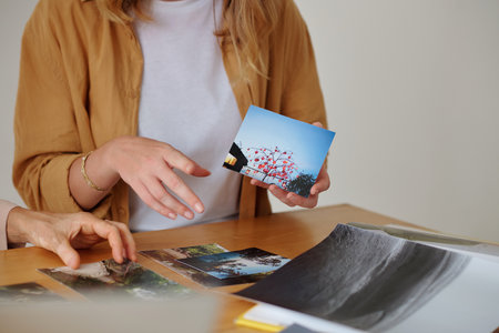 Close-up of young woman showing photo of autumn tree to colleague during discussion of new items and choosing some of them for exhibitionの写真素材