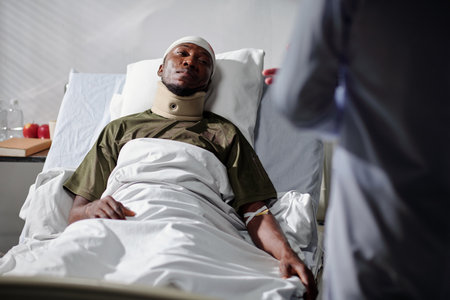 African American soldier with injury lying on bed in hospital and listening to the doctorの写真素材