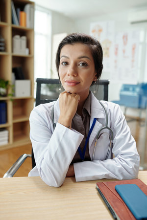 Portrait of smiling female general practitiner sitting at desk and looking at cameraの写真素材
