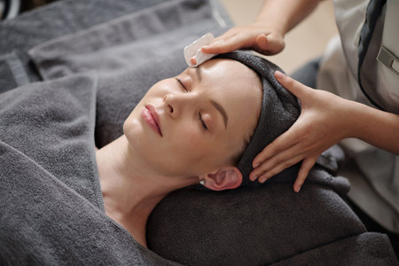 Cosmetologist wiping off makeup from face of young woman