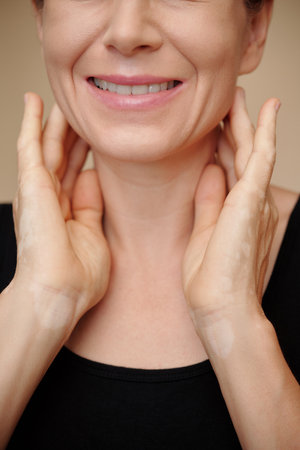 Cropped image of smiling mature woman massaging her neck to reduce swellingの写真素材