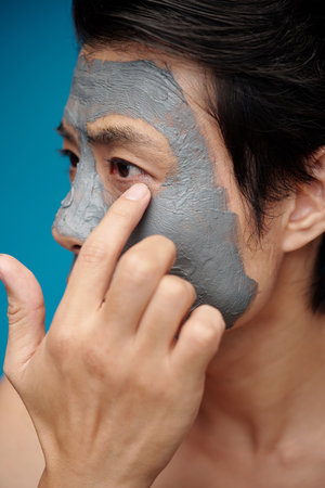 Man checking if clay mask dried on his face and it is time to wash it offの写真素材