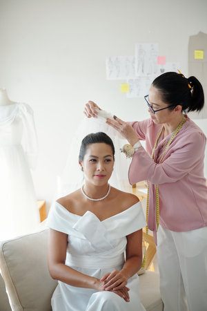 Wedding salon worker helping bride to wear veilの写真素材
