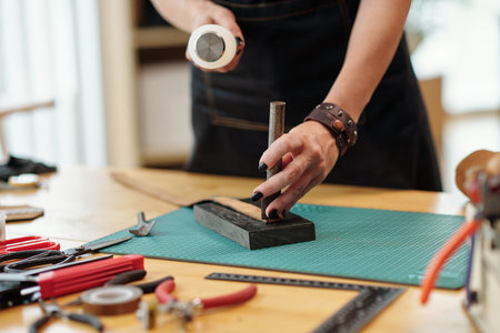 Hands of creative young woman stamping leather belt in her studioの写真素材
