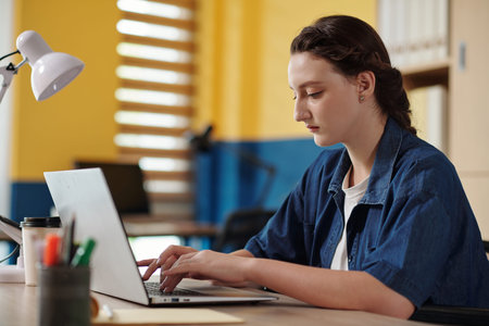 Serious young woman working on laptop in office