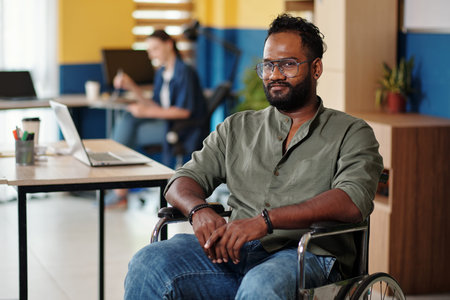 Portrait of Indian businessman sitting in wheelchair and smiling at cameraの写真素材