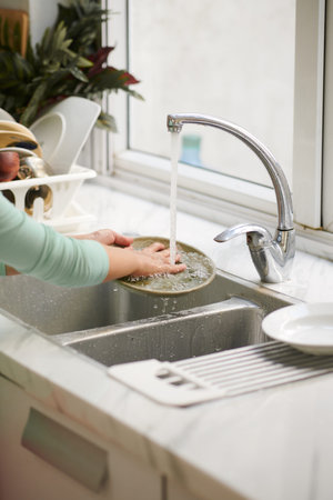 Hands of preteen girl rinsing dishes under tap waterの写真素材