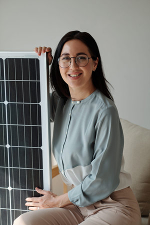 Portrait of smiling young woman sitting next to solar panel she boughtの写真素材