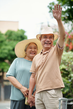Cheerful senior man waving with hand when catching taxi to hotelの写真素材