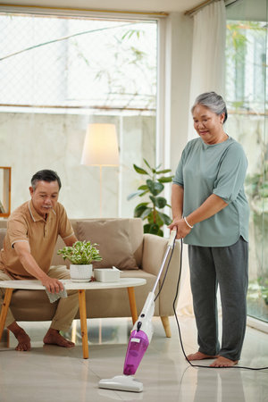 Senior couple cleaning apartment, vacuum cleaning floor and wiping dustの写真素材