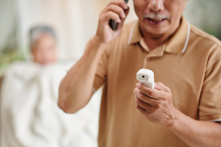 Aged man calling ambulance after measuring body temperature of his wifeの写真素材