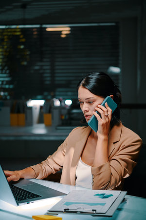 Young entrepreneur answering phone call from manager living in another country late at nightの写真素材