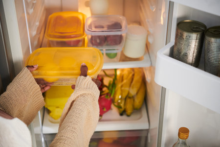 Woman taking plastic container with fresh fruits from fridgeの写真素材