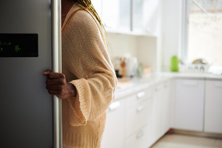 Cropped image of woman opening refrigerator in kitchen to take something to eatの写真素材