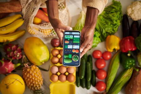 Woman holding smartphone with food delivery application over table with fresh groceriesの写真素材