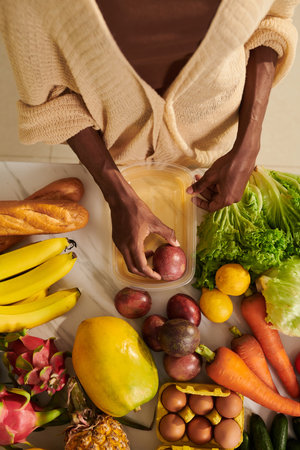 Woman packing fresh fruits and vegetables in plastic containers to store in fridgeの写真素材