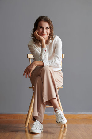 Positive elegant mature woman sitting on chair and smiling at camera