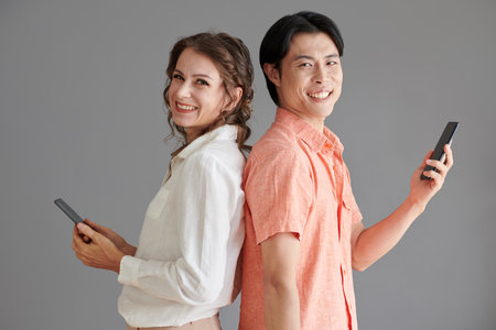 Cheerful man and woman standing back to back when texting friends or colleaguesの写真素材