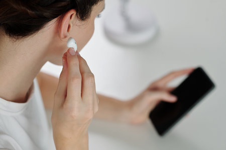 Woman inserting earbuds to listen to voice message from coworker