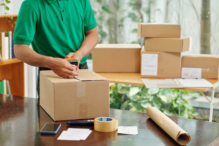 Mail worker sealing cardboard boxes before shipping goods to customerの写真素材